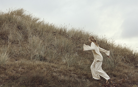 A nordic woman running up a beachside hill with her hair flowing in the wind